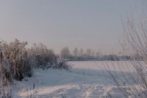 Serene winter landscape with snow-covered fields and frozen river under a clear sky.